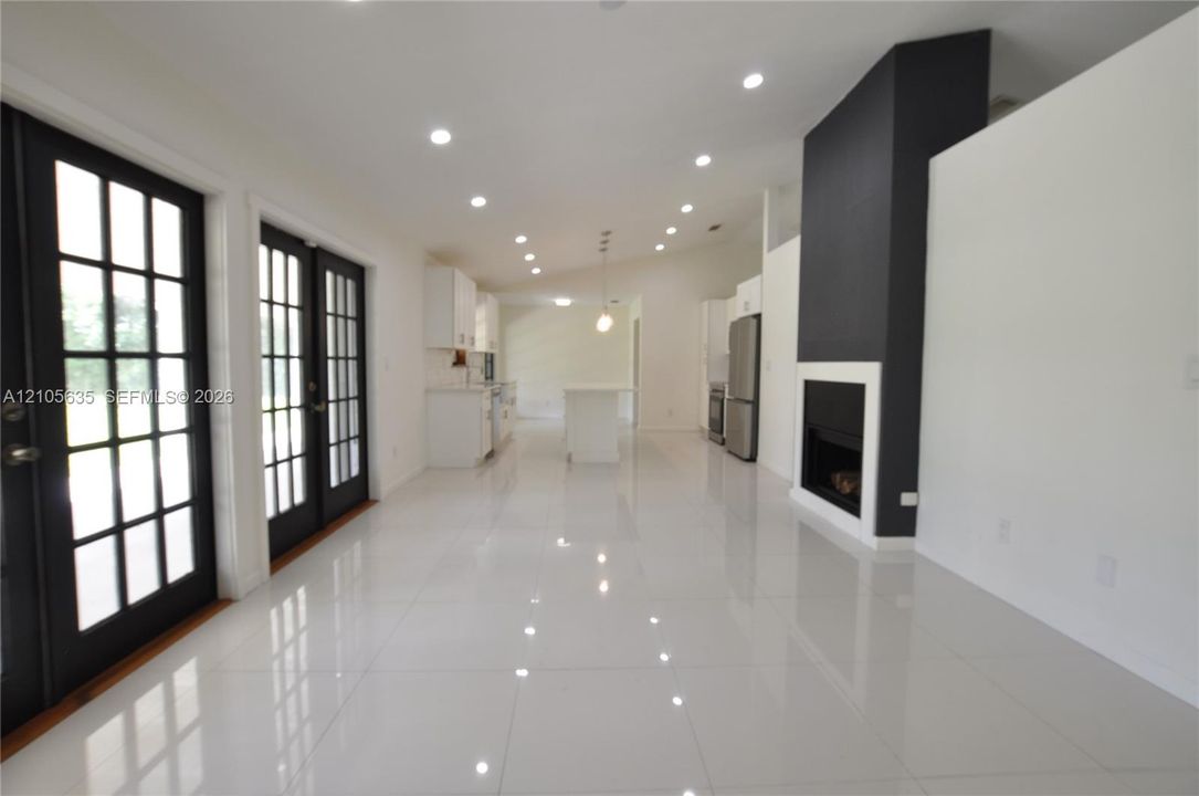 Open interior featuring white tile flooring, recessed lighting, double French doors with black frames, and a floor-to-ceiling fireplace with a contrast hearth