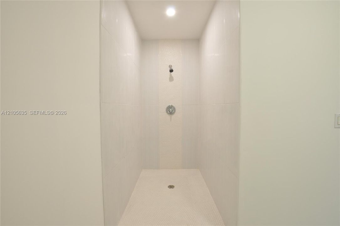 Walk-in shower featuring large-format wall tile, mosaic tile accent inlay, circular shower head, and recessed ceiling lighting