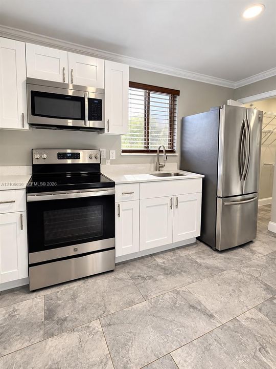Kitchen featuring white shaker-style cabinetry, quartz countertops, stainless steel appliances, a stainless steel undermount sink with a gooseneck faucet, and large-format tile flooring