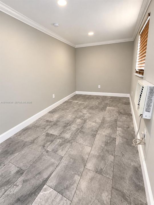 Neutral-toned interior featuring stone-finish tile flooring, crown molding, recessed lighting, and a wall-mounted climate control unit