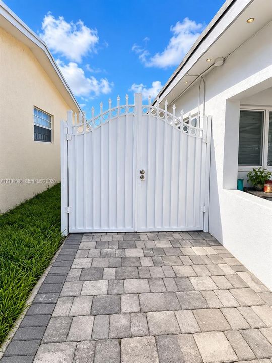 White metal arched double gate featuring decorative finials and multi-tone concrete paver flooring