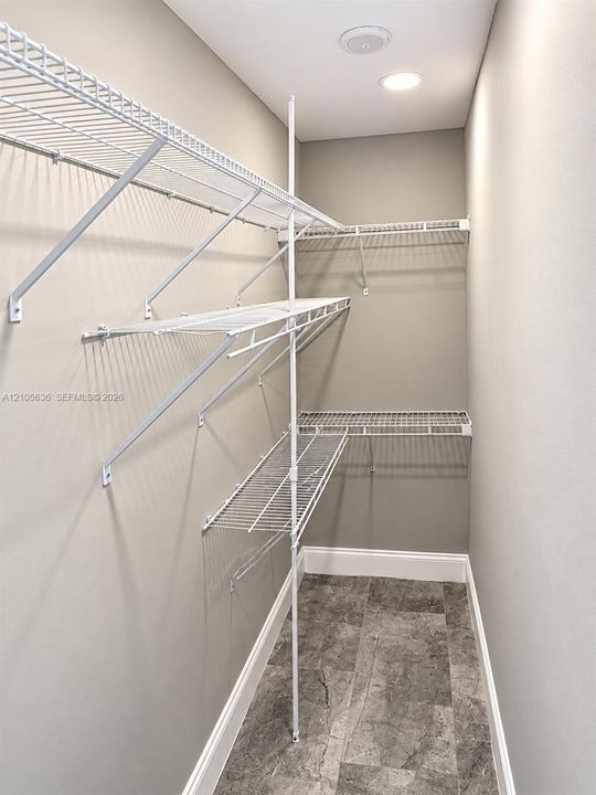 Walk-in storage area featuring multi-level white wire shelving, recessed ceiling lighting, and stone-finish flooring
