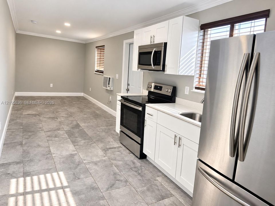 Kitchen featuring white shaker-style cabinetry, stainless steel appliances, solid-surface countertops, and large-format tile flooring