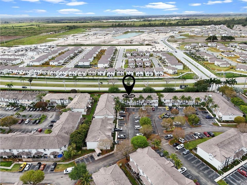 Aerial perspective of multi-family community featuring light-colored shingled roofs, stucco exterior finish, mature palm tree landscaping, and paved surface parking