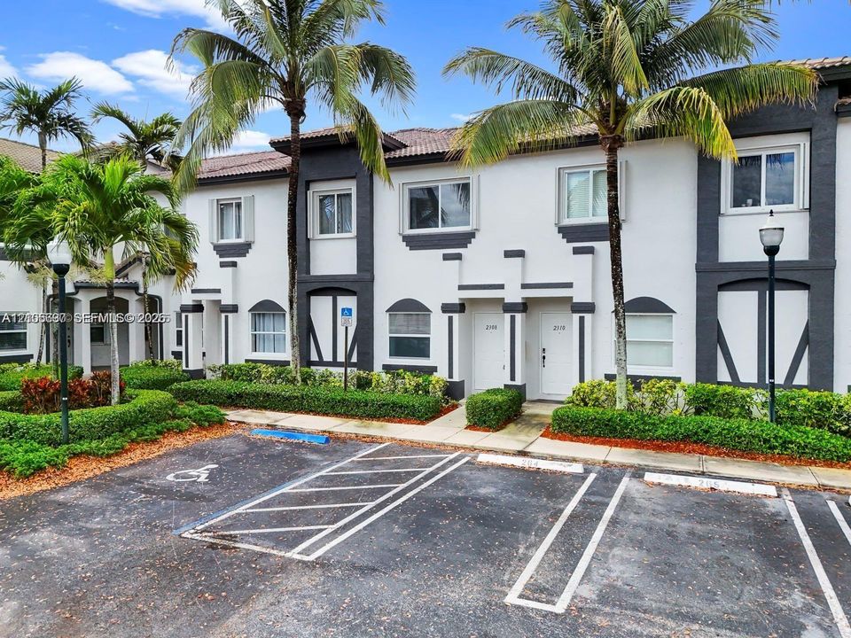 Stucco exterior featuring contrasting dark trim, tile roof, mature palm trees, and manicured shrubbery