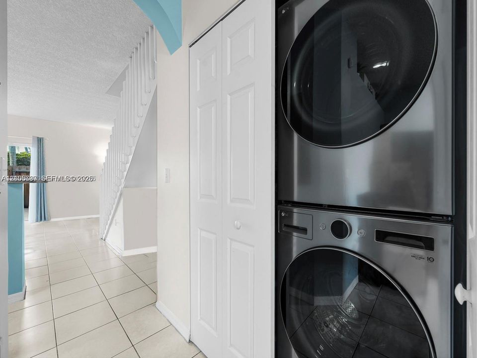 Stacked stainless steel laundry appliances, ceramic tile flooring, and white louvered closet doors