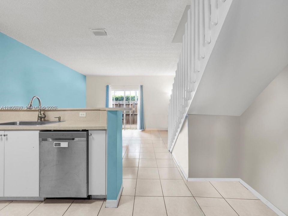 Kitchen featuring a peninsula, stainless steel dishwasher, stainless steel faucet, tile flooring, and a staircase with white vertical balusters