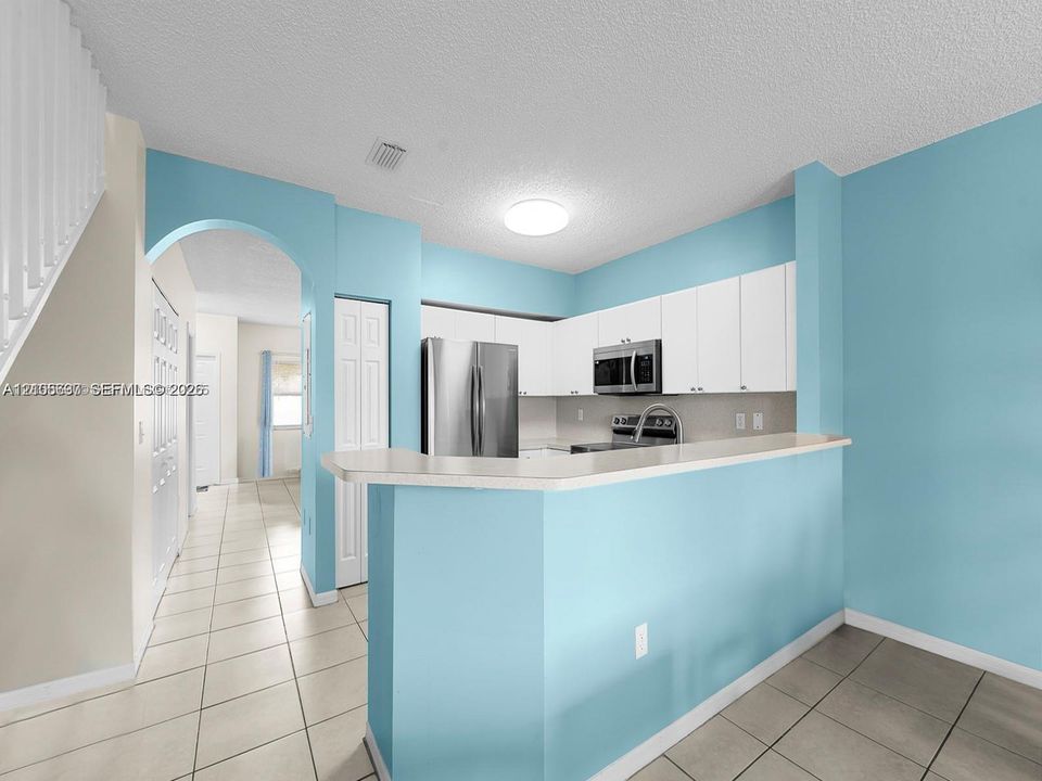 Kitchen featuring white cabinetry, stainless steel appliances, solid-surface breakfast bar, and tile flooring throughout