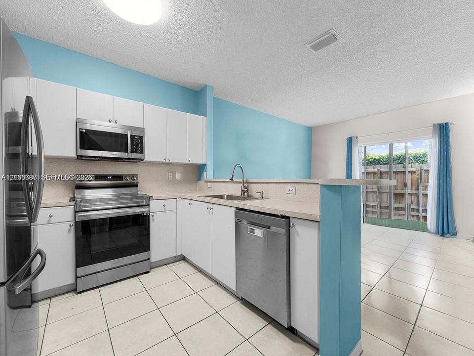 Kitchen featuring white cabinetry, stainless steel appliances, neutral stone-finish countertops, and ceramic tile flooring