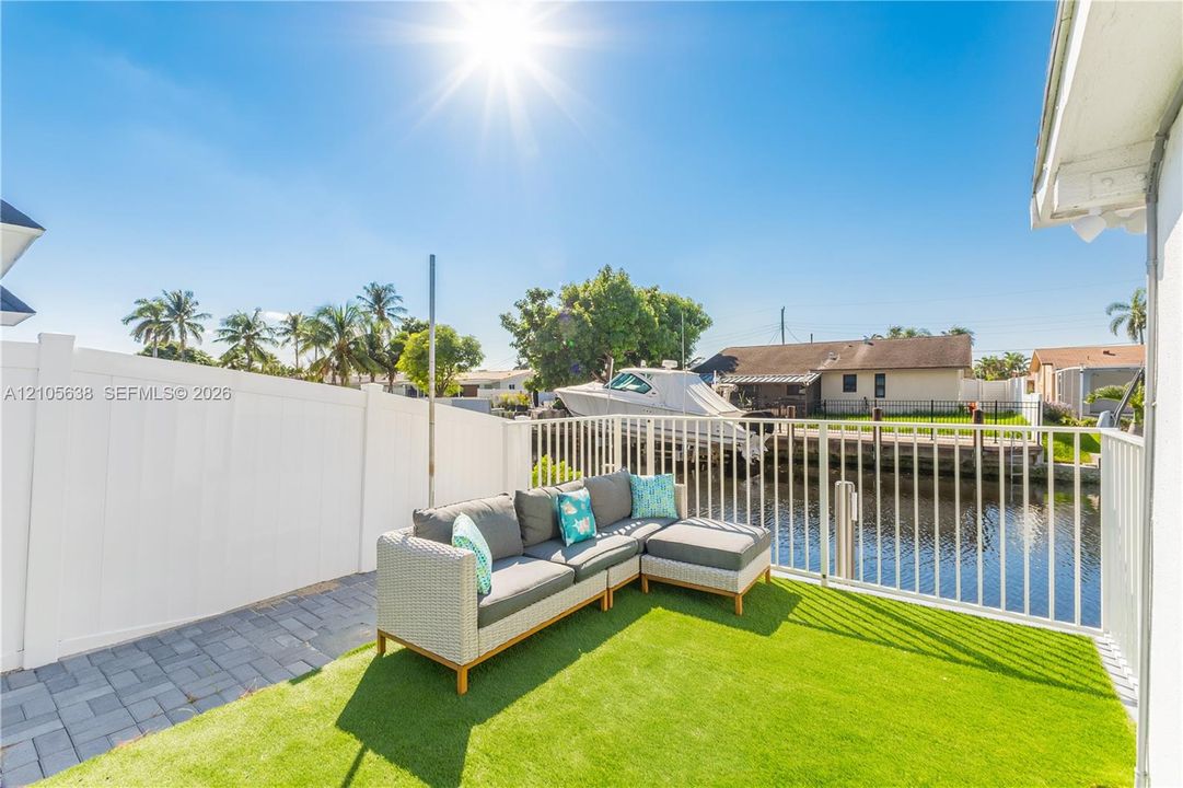 Waterfront patio featuring synthetic turf, interlocking paver hardscaping, and a white privacy fence with aluminum perimeter railing