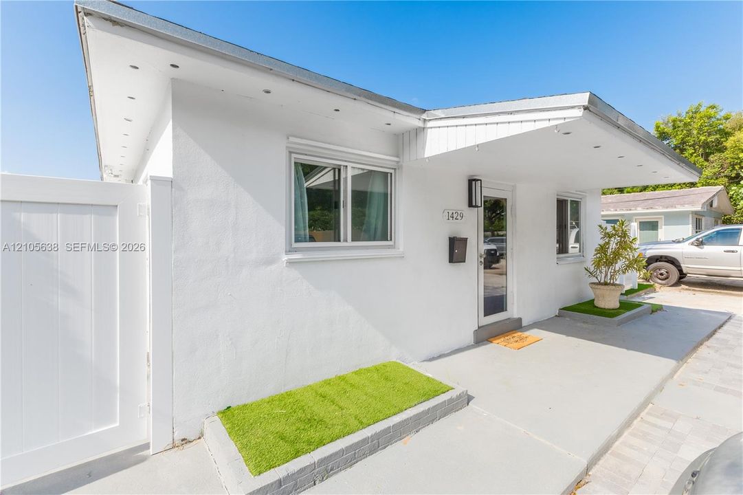 Exterior featuring smooth white stucco finish, extended roof overhang with integrated lighting, dual-pane windows, and a dedicated concrete porch area with built-in planter beds