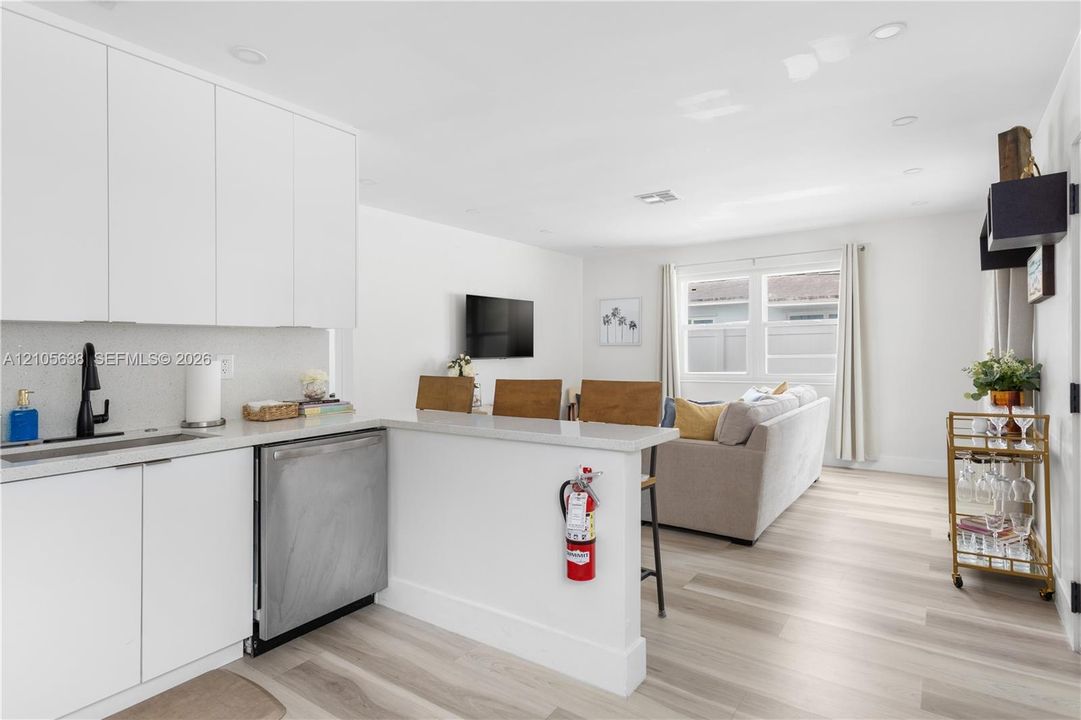 Modern kitchen featuring sleek white cabinetry, a light-toned countertop, a built-in stainless steel dishwasher, a matte black faucet, and wood-finish flooring