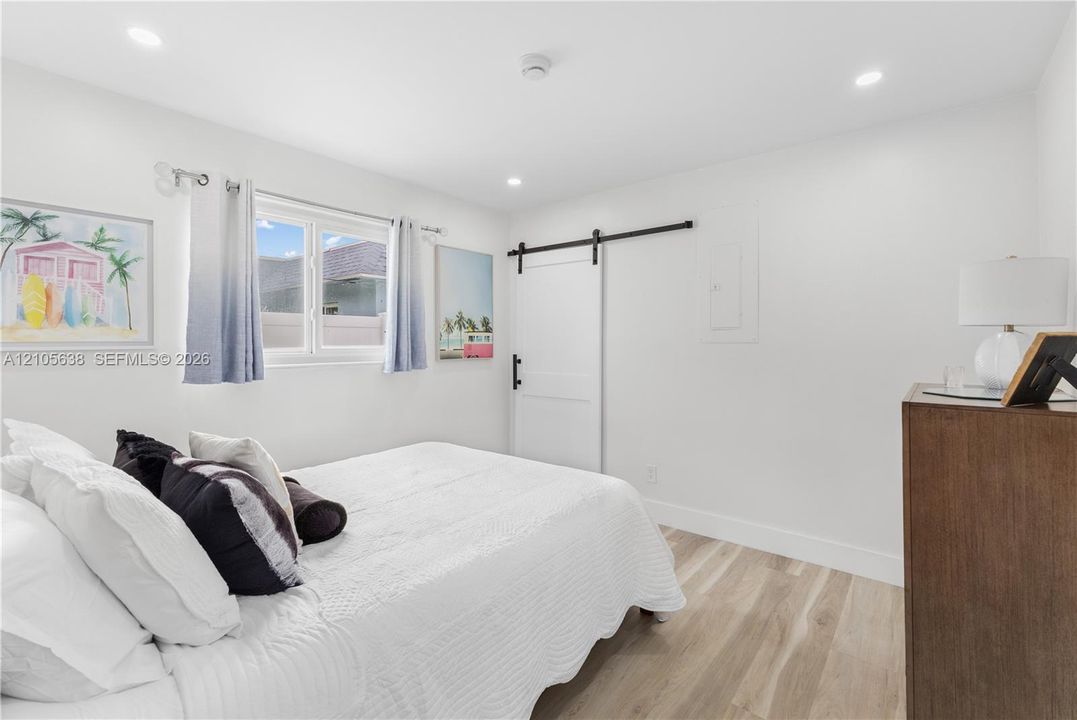 Wood-finish flooring, recessed lighting, and a white sliding barn door with matte black hardware