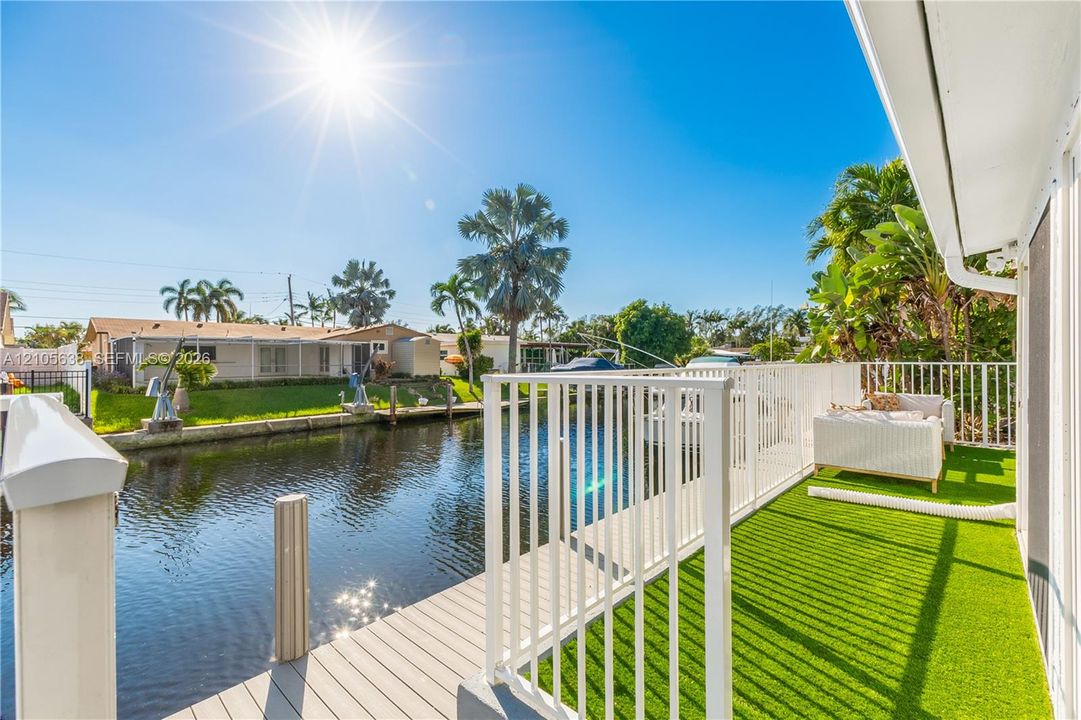 Waterfront deck featuring a synthetic turf surface, a neutral-toned composite boardwalk, and perimeter white metal railing