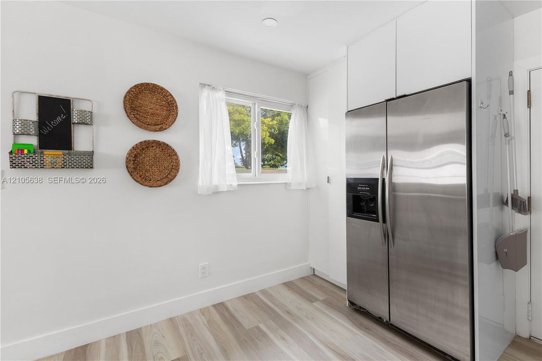 Stainless steel side-by-side refrigerator, white full-height cabinetry, and wood-finish flooring