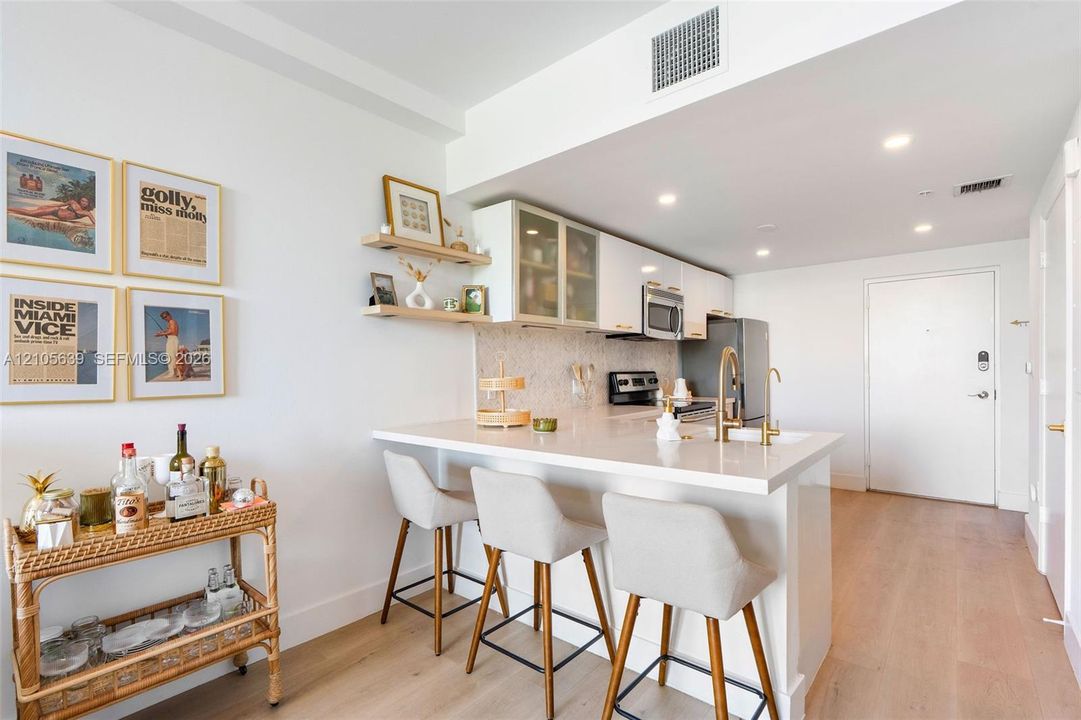 Kitchen featuring white flat-panel cabinetry, quartz countertops, integrated stainless steel appliances, open wood shelving, and wood-finish flooring