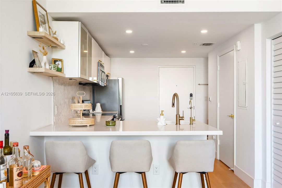 Kitchen featuring quartz countertops, white cabinetry, recessed lighting, wood-finish flooring, and floating wall shelves