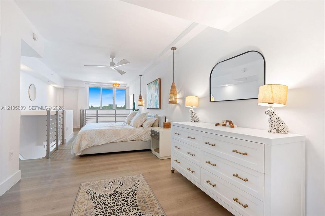 Wood-finish flooring, recessed ceiling lighting, three-blade ceiling fan, arched wall-mounted mirror, and metal railing partition