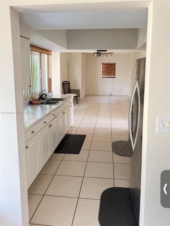 Kitchen featuring white cabinetry, solid-surface countertops, dual-basin stainless steel sink, and ceramic tile flooring