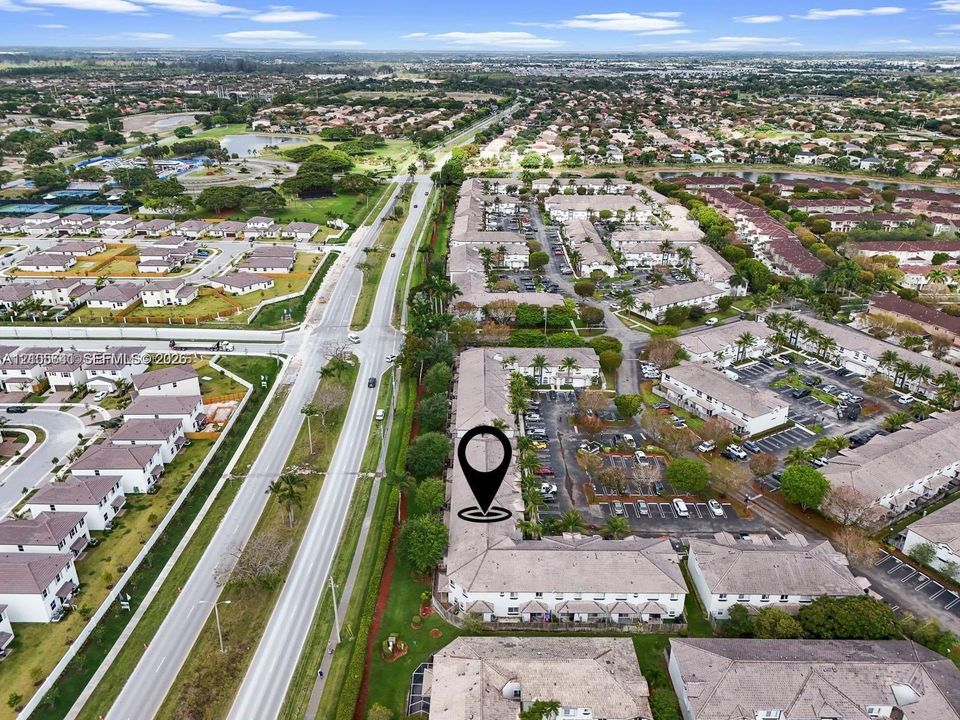 Aerial perspective featuring residential multi-unit structures, integrated paved surface parking, mature landscaping, and multi-lane thoroughfares