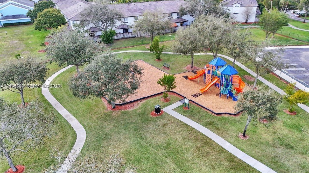 Community recreational area featuring a playground with slides, paved walking paths, mature trees, and landscaped green space