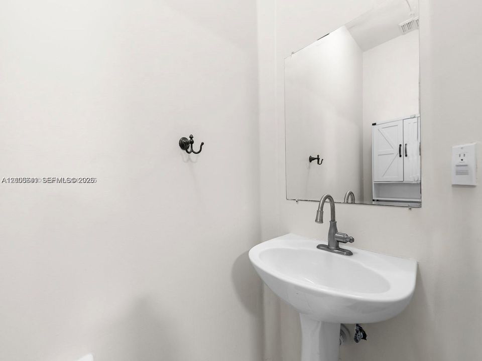 White pedestal sink with a metallic high-arc faucet, wall-mounted mirror, and decorative wall-mounted hardware
