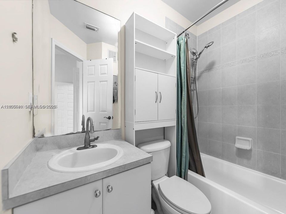 Bathroom featuring a vanity with a solid-surface countertop, an oval under-mount sink, integrated tall cabinet storage, and a tiled shower-tub combination with a handheld shower fixture