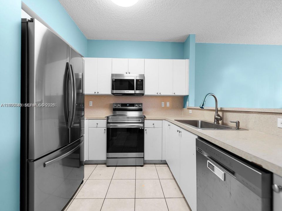 Kitchen featuring white cabinetry, stainless steel appliances, neutral solid-surface countertops, a stainless steel undermount sink with a gooseneck faucet, and tile flooring