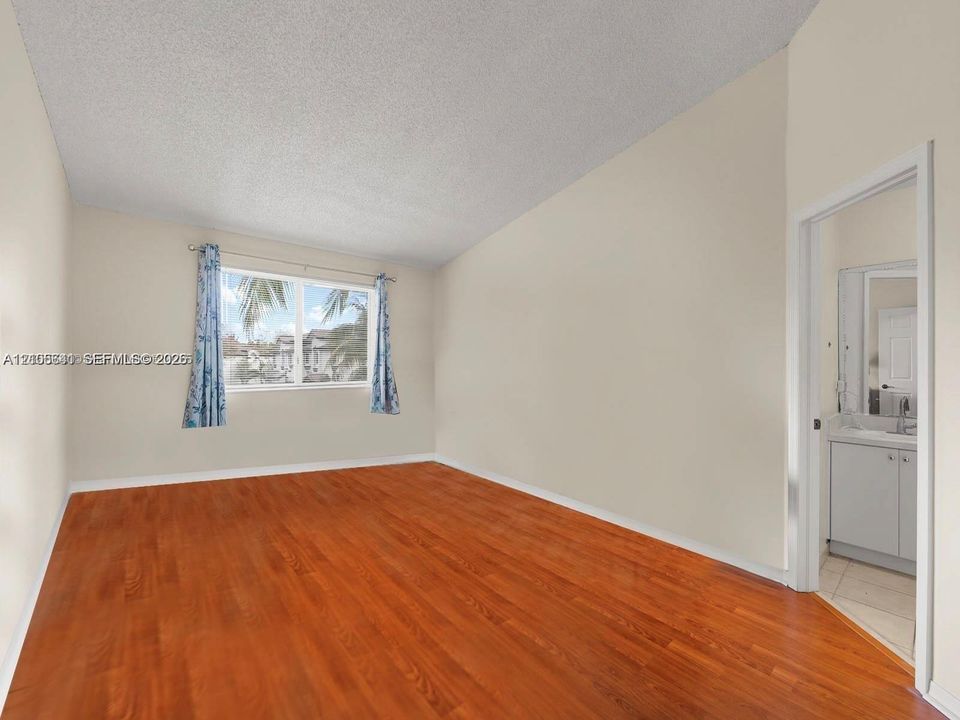 Room featuring wood-finish flooring, textured ceiling, and a window with exterior residential surroundings
