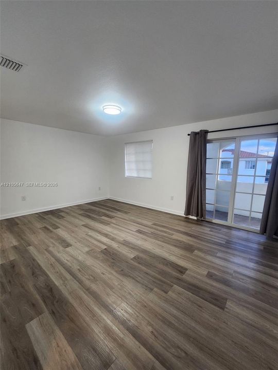 Room featuring wood-finish flooring, white walls, flush-mount ceiling lighting, a single window, and sliding glass doors
