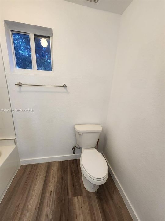 Bathroom featuring wood-finish flooring, a white porcelain toilet, a sliding window, and a wall-mounted metal towel bar