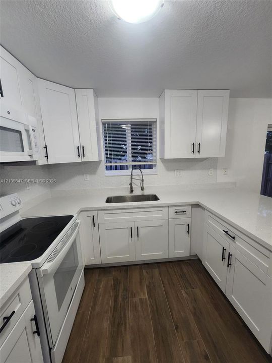 Kitchen featuring white shaker-style cabinetry, solid-surface countertops, wood-finish flooring, undermount stainless steel sink, and a pull-down faucet