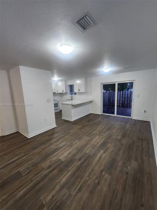 Open-concept interior featuring wood-finish flooring, white cabinetry, a breakfast bar, and glass sliding doors