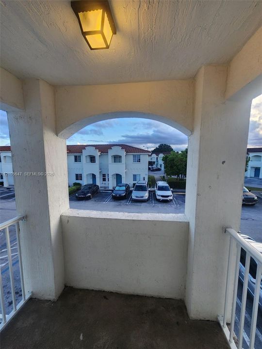 Covered balcony featuring a white metal railing, stucco walls, an arched opening, and a flush-mount exterior light fixture