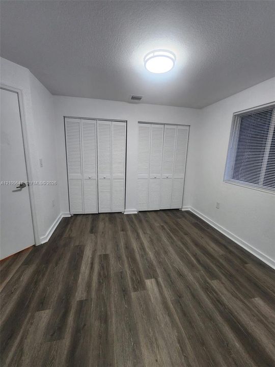 Room featuring wood-finish flooring, dual bi-fold door closets, and a flush-mount ceiling light fixture