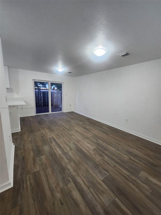 Wood-finish flooring, white walls, flush-mount ceiling lighting, and glass sliding door access to exterior grounds