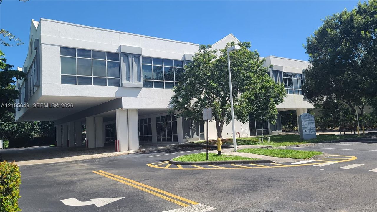 Two-story exterior featuring a white stucco facade, expansive grid-pattern glass windows, a cantilevered building section, and covered ground-level parking
