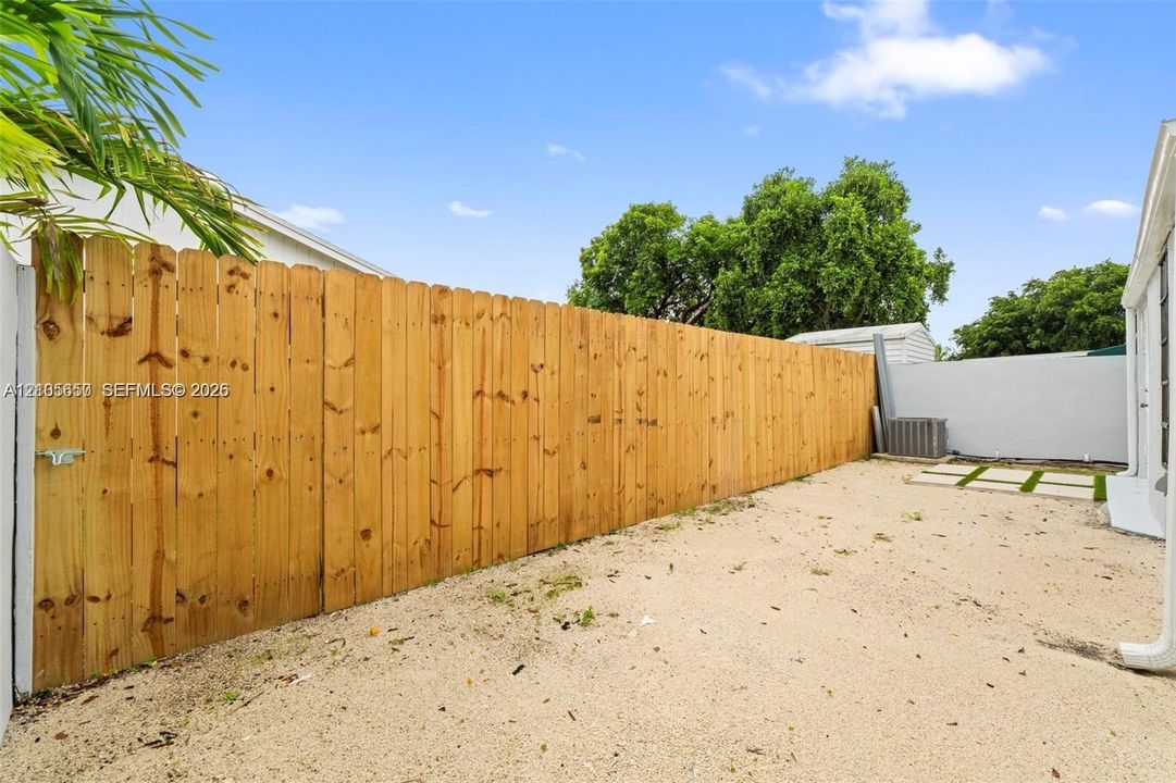Side yard featuring a tall wood-panel privacy fence, graveled ground surface, and integrated paver stones