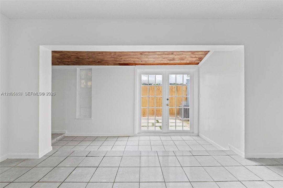 Interior space featuring white ceramic tile flooring, wood-plank ceiling treatment, and white-framed French doors