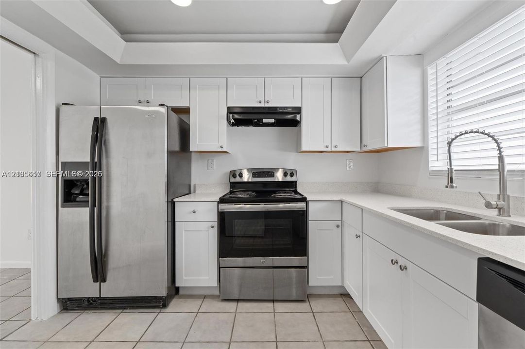 Kitchen featuring white cabinetry, stone-finish countertops, stainless steel appliances, tray ceiling, and tile flooring