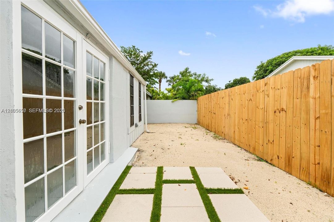 Exterior side area featuring glass-paned French doors, concrete paver patio with turf inlay, gravel ground cover, and a wood privacy fence