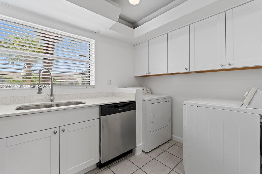 Utility room featuring white cabinetry, a light-toned stone-finish countertop, an integrated sink with a gooseneck faucet, a stainless steel dishwasher, and tile flooring