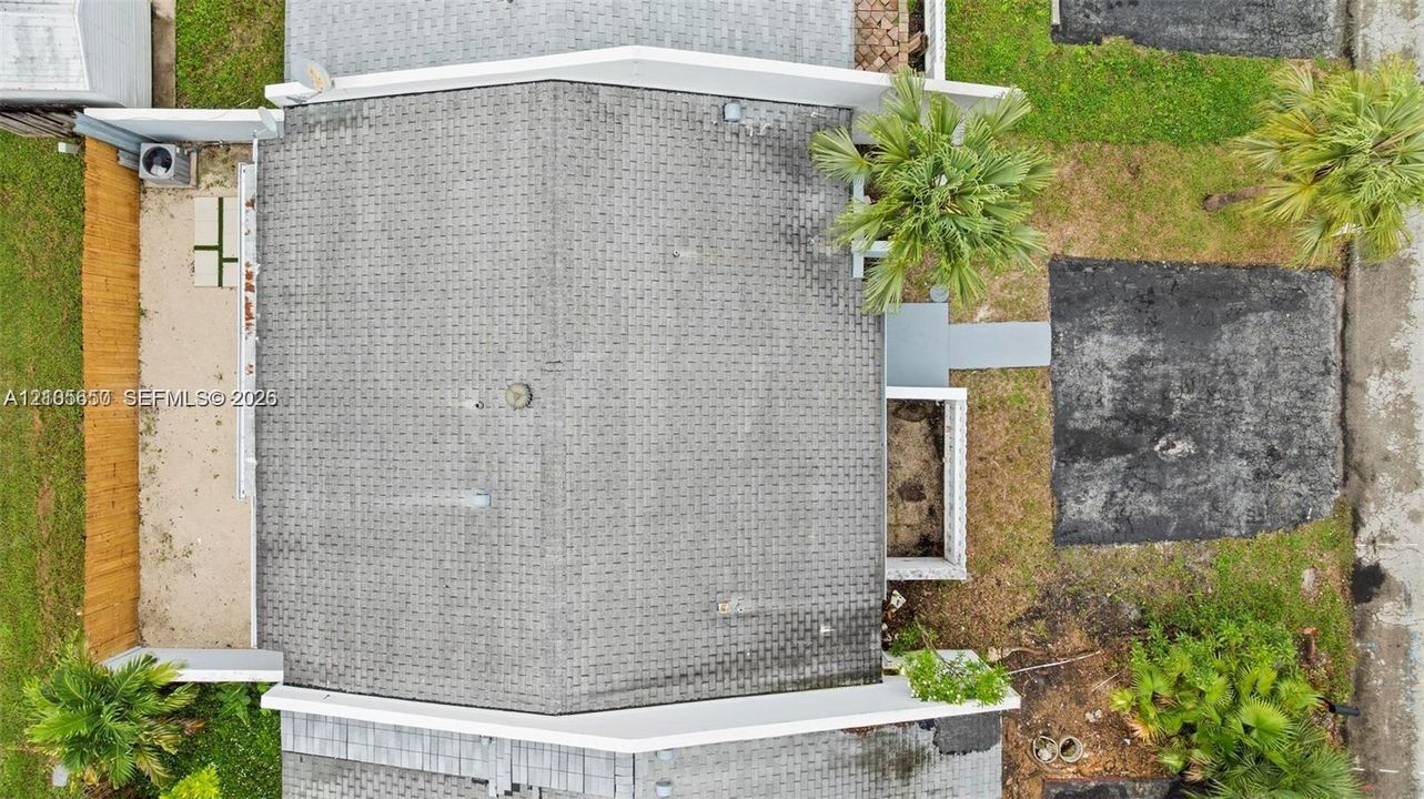 Aerial perspective of the property featuring a shingle roof, paved driveway, enclosed side yard, and established palms