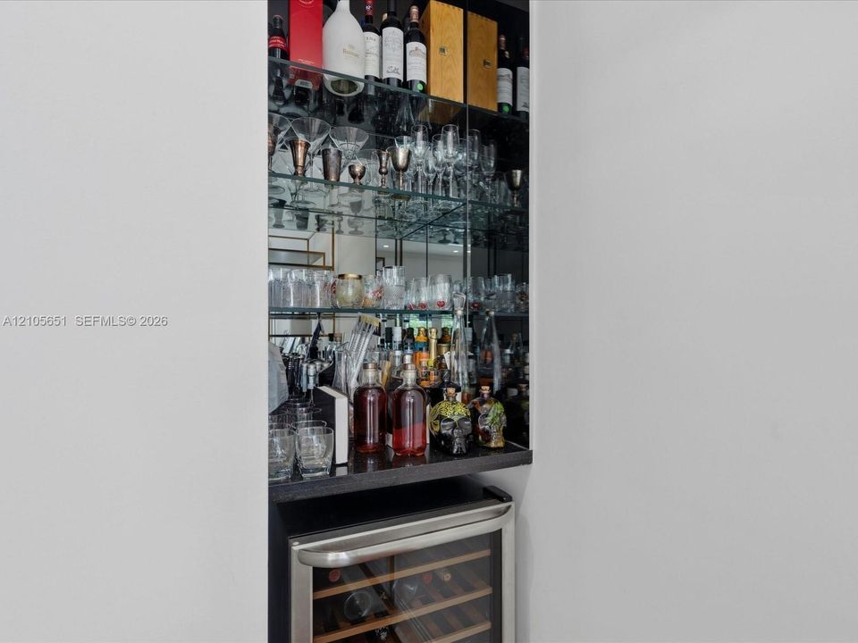 Built-in recessed display cabinet featuring mirrored backing, glass shelving, a dark stone countertop, and an integrated stainless steel wine refrigerator