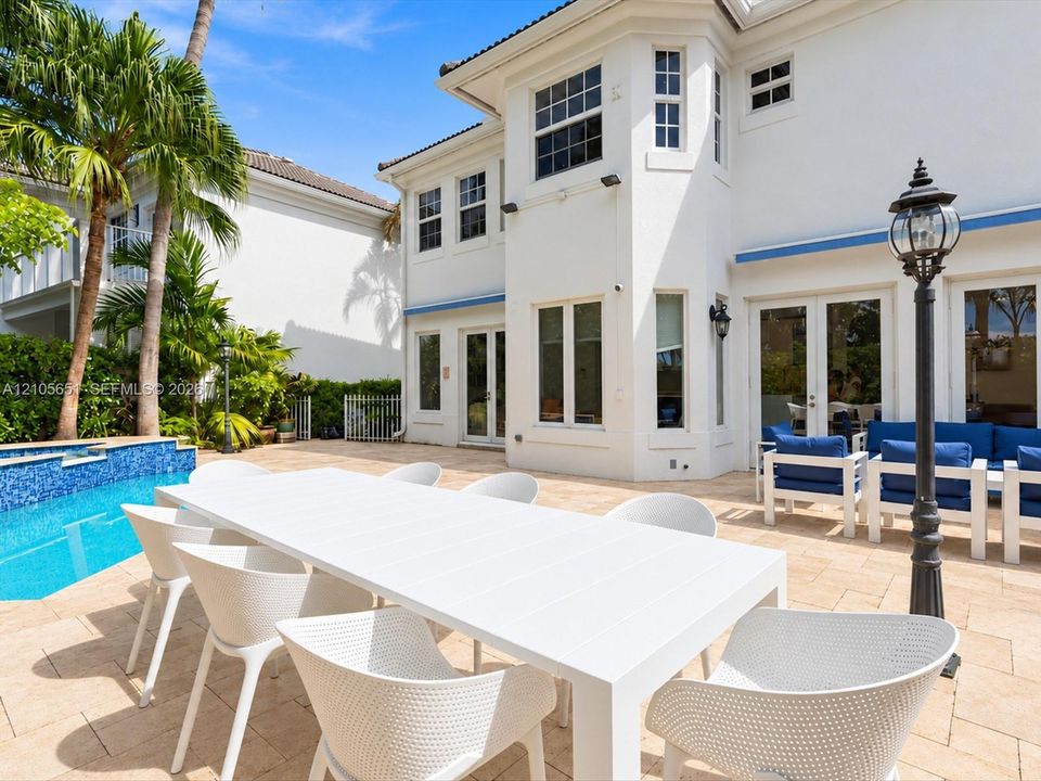 Outdoor patio featuring paver flooring, a swimming pool with tile finish, multiple sets of glass-paneled double doors, and a decorative post lamp