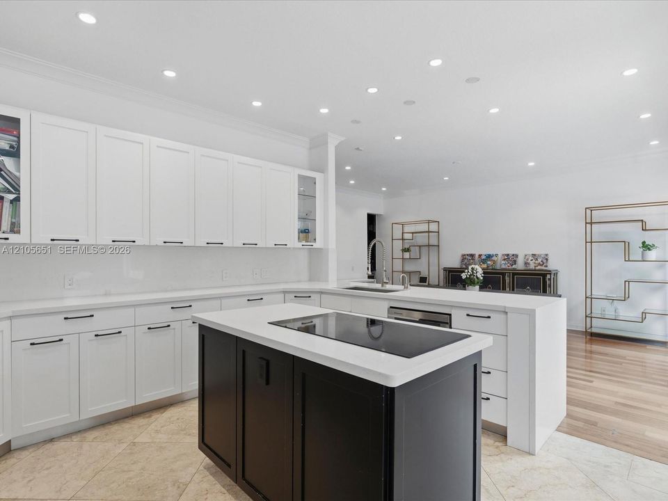 Kitchen featuring white cabinetry with glass-front display panels, central island with a contrasting dark finish, integrated stovetop, recessed lighting, and stone flooring