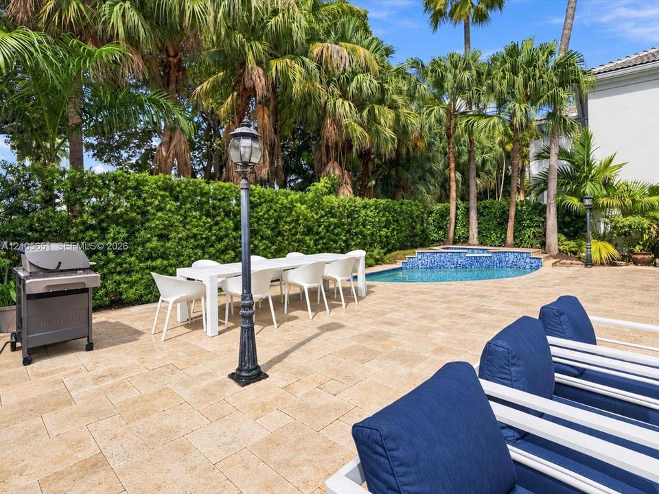 Outdoor living area featuring a stone-paver patio, a pool with a tile-accented spa, and perimeter hedging