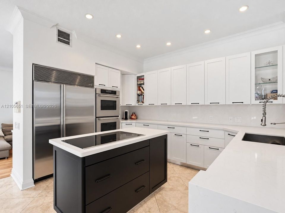 Kitchen featuring white shaker-style cabinetry, contrasting black center island, built-in stainless steel double wall oven, integrated refrigerator, and solid-surface countertops
