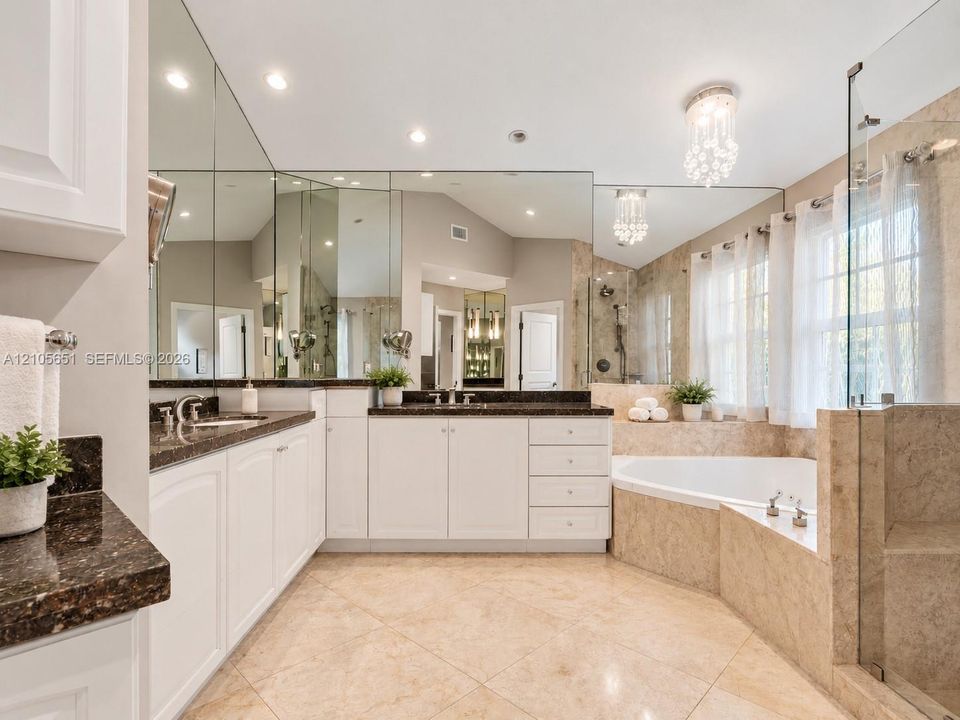 Bathroom featuring a double vanity with stone countertops, tiled soaking tub, walk-in glass-enclosed shower, wall-to-wall mirrors, and crystal light fixtures