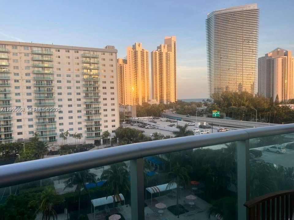 Elevated balcony featuring a glass panel railing and a panoramic perspective of the cityscape and coastal horizon